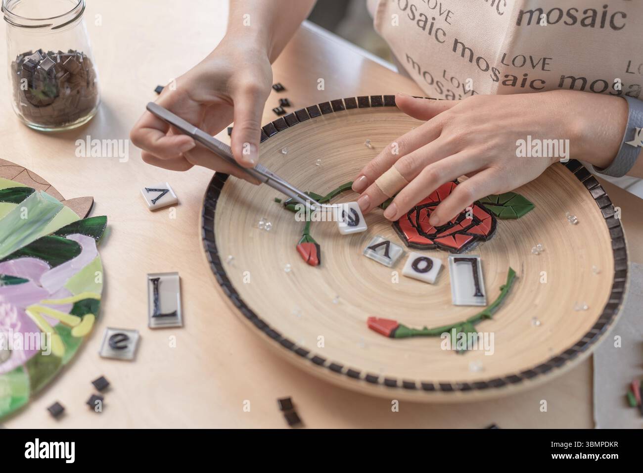 Poste de travail d'un maître de la mosaïque : mise en forme d'un élément de la mosaïque sur la table. Le maître établit sur une plaque en mosaïque fait main de maître Banque D'Images