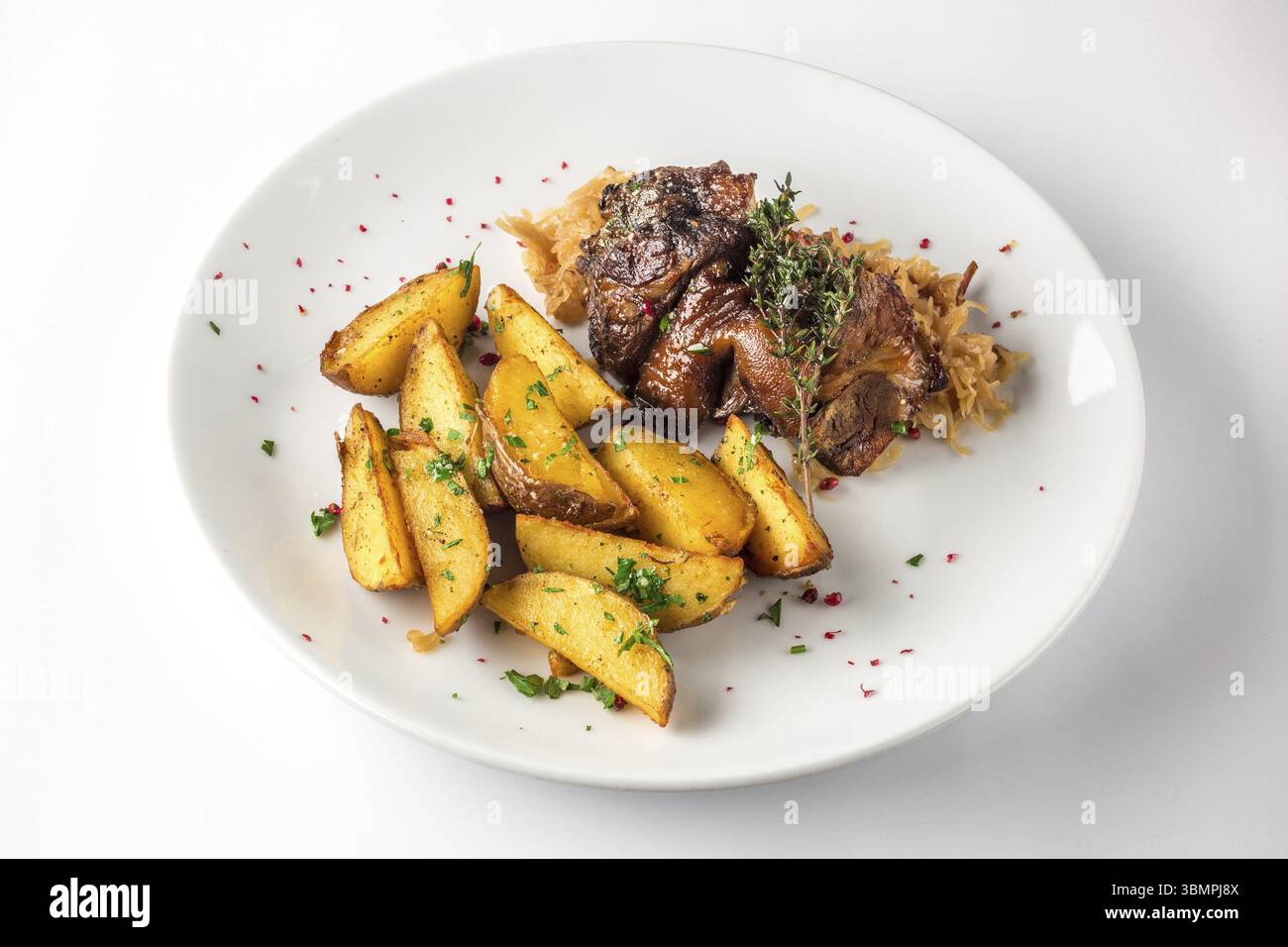 De délicieuses ailes de canard grillées avec des pommes de terre et du chou cuit sur une assiette blanche. Vue de dessus sur fond blanc Banque D'Images