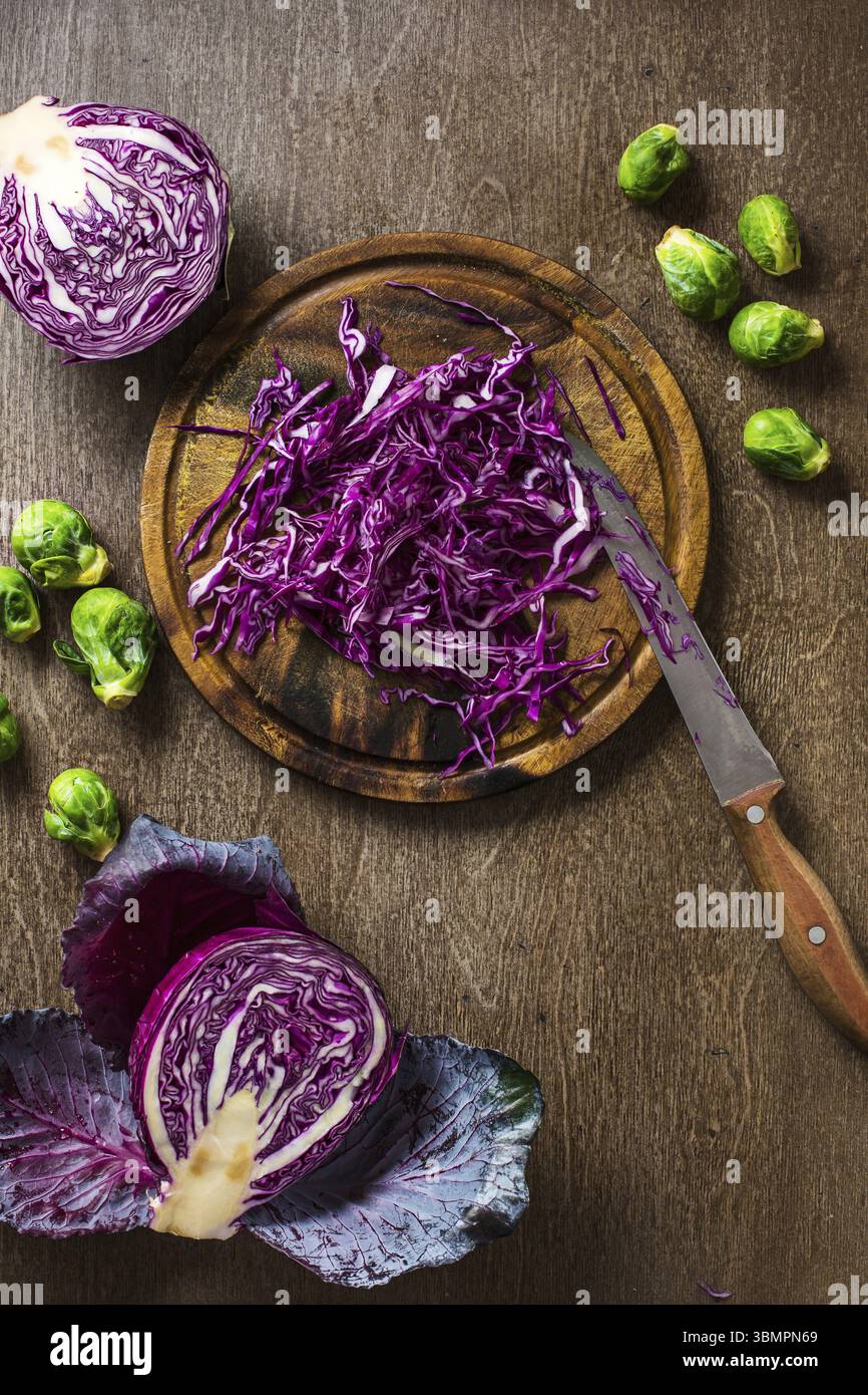 Un choux rouge en tranches et des choux de bruxelles sur fond d'ardoise et de comptoir en bois, sur le plateau avec un couteau Banque D'Images