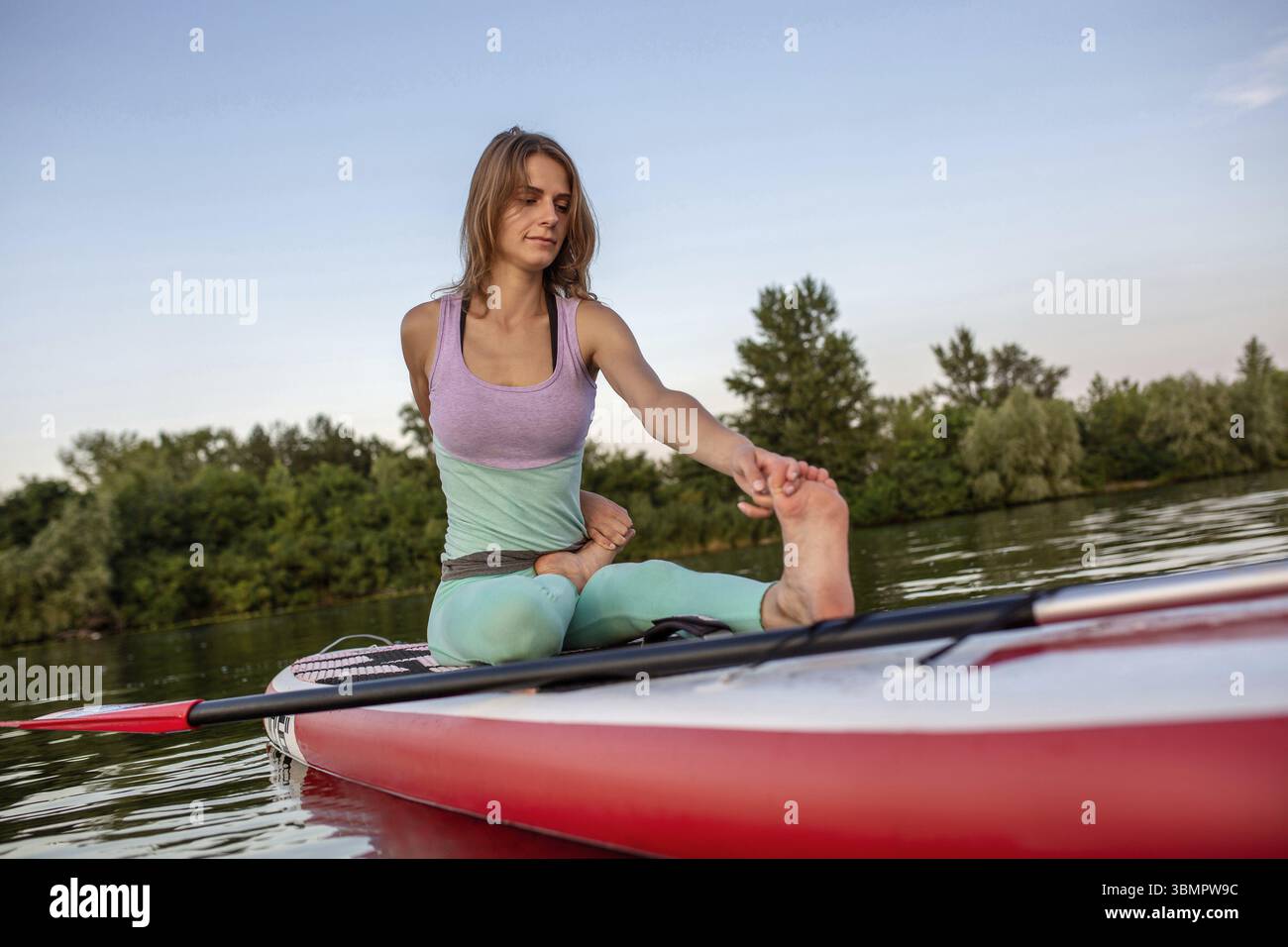 Jeune femme assise sur le paddle board, la pratique du yoga. Faire du yoga sur l'exercice du Conseil sup, l'été reste active. Exercice de souplesse et stretchi Banque D'Images