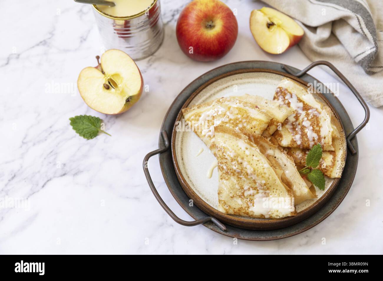 Célébration de la journée des crêpes, petit déjeuner sain. Crêpes sucrées maison avec pommes et lait condensé sur une table en marbre. Copier l'espace Banque D'Images