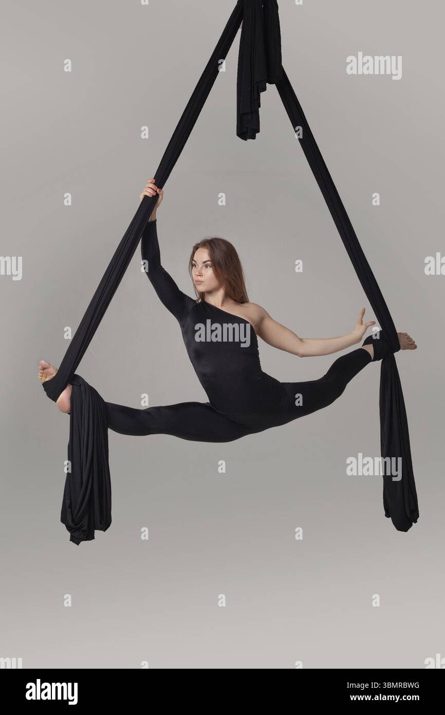 Performance de gymnaste sur une toile noire. Magnifique fille dans un costume de sport sombre fait une ficelle suspendue à une corde et regardant loin dans un studio isolé o Banque D'Images