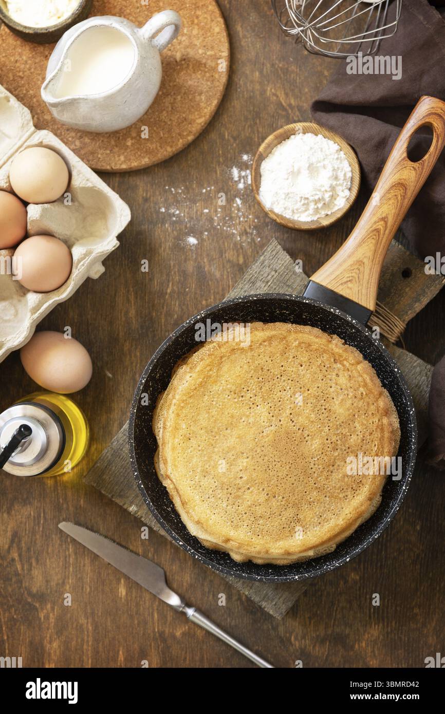 Fêtez le jour du Pancake, cuisinez un petit déjeuner sain. Crêpes ou crêpes maison délicieuses dans une poêle et ingrédients sur une table rustique. Vue de Banque D'Images