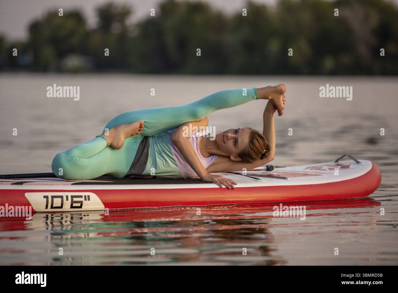 Sporty woman in yoga position sur le paddleboard, faisant du yoga sur le conseil sup, l'exercice de flexibilité et étirement des muscles. Woman practicing yoga on th Banque D'Images