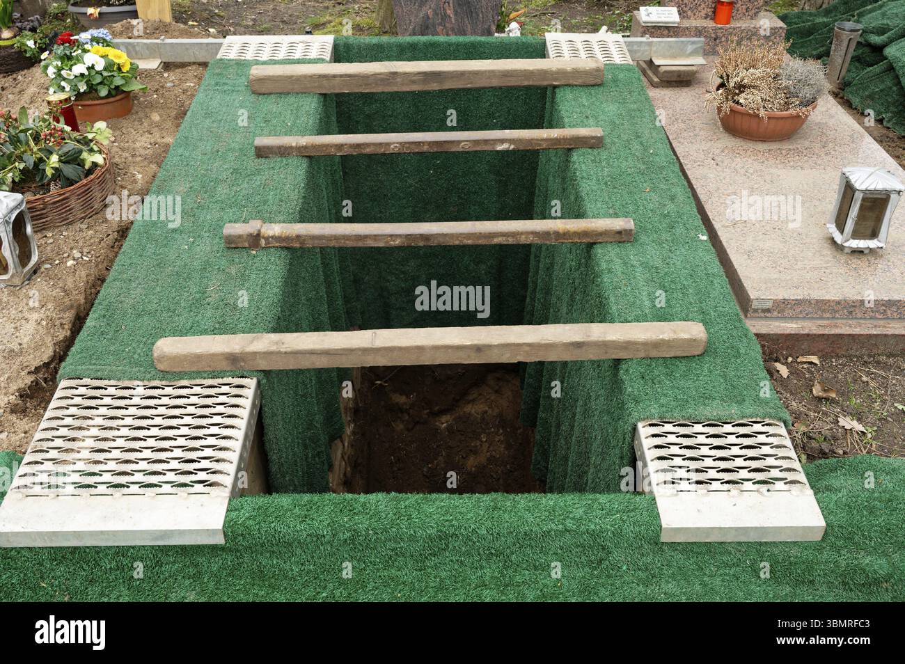 Une tombe creusée avec des nattes d'herbe verte juste avant un enterrement dans un cimetière Banque D'Images