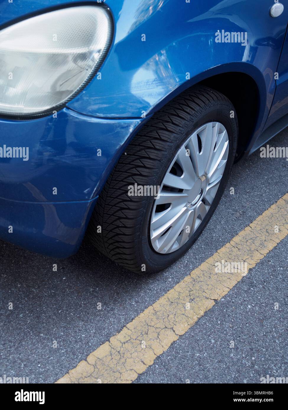 Cremona, Italie 11 juin 2025 roue avant droite d'une Toyota Yaris série XP10 bleue garée légèrement au-dessus de la ligne jaune dans un parking, soulignant Banque D'Images
