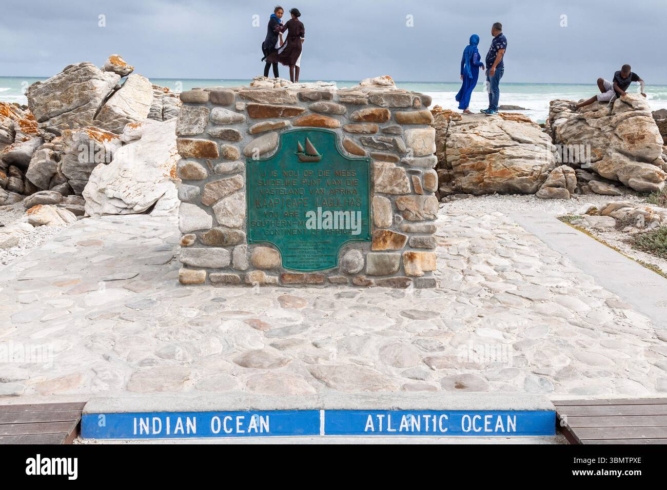 Touristes à la balise du cap Agulhas marquant la confluence des océans Indien et Atlantique à la pointe sud de l'Afrique par une journée orageuse Banque D'Images