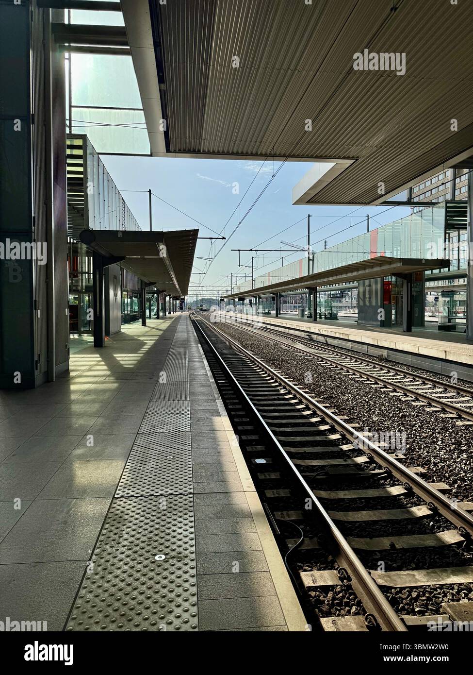 Quai de chemin de fer vide dans une gare moderne avec toit en acier et voies parallèles. L'image capture un moment calme sans trains ni passagers. Banque D'Images