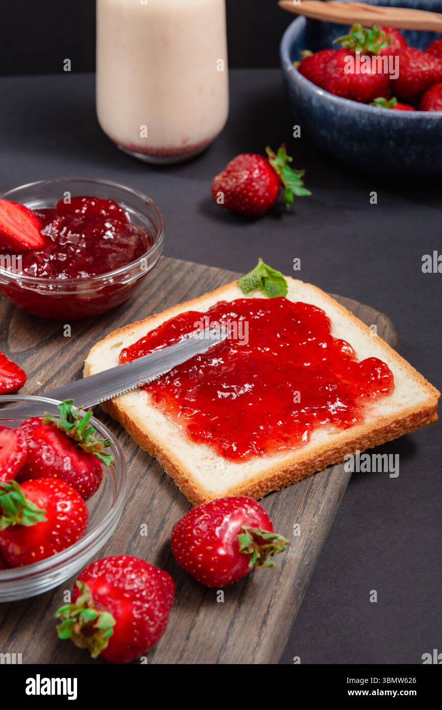 Confiture de fraises maison sur pain grillé, entouré de fraises fraîches, idées de petit déjeuner, conserves maison Banque D'Images
