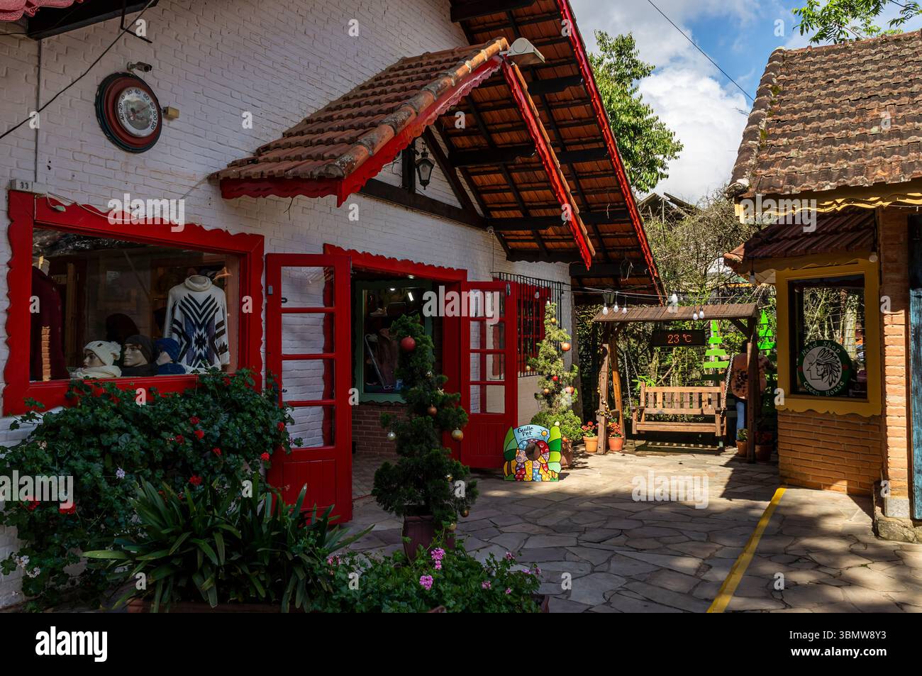 Charmante cour dans le centre commercial Celeiro, sur l'avenue Monte Verde, avec des boutiques, un décor festif et des sièges extérieurs sous le ciel ensoleillé. Banque D'Images