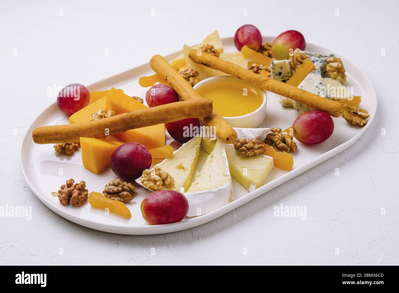 Nature morte, plateau de fromage au miel, noix et raisins rouges Banque D'Images