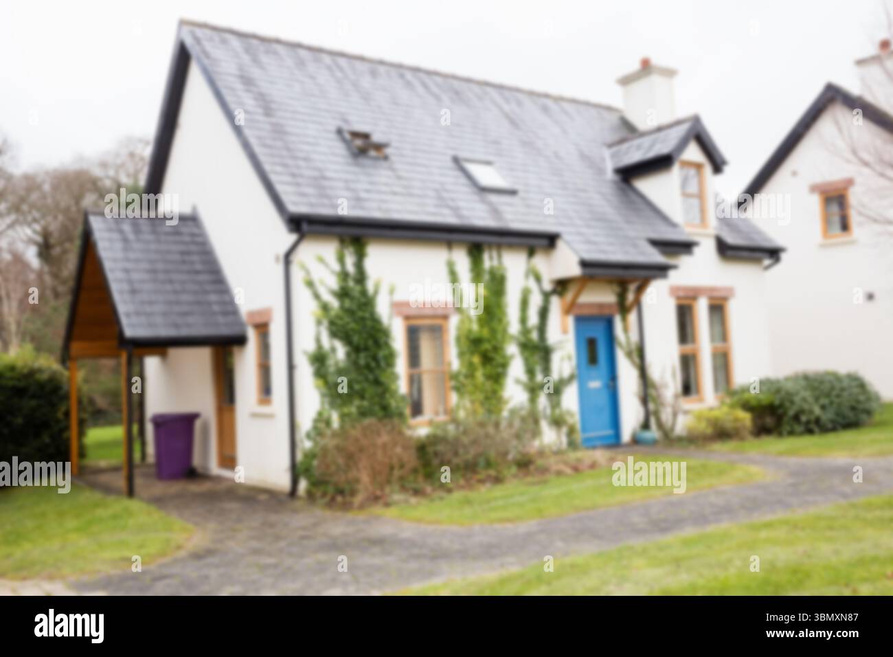 Maison blanche de style cottage se tient près de l'allée courbe, montrant la porte bleue, le toit en ardoise et le porche Banque D'Images