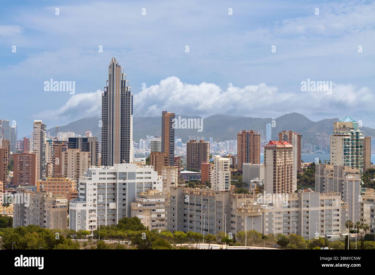 Paysage urbain de Benidorm avec de hauts gratte-ciel, la côte méditerranéenne et des montagnes lointaines sous un ciel partiellement nuageux par une journée ensoleillée. Banque D'Images