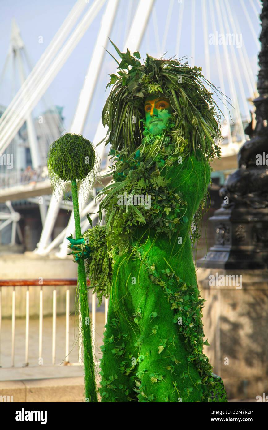 Artiste habillé comme une statue verte vivante avec le personnel près de Millennium Bridge sur South Bank, Londres - mêlant art, nature et vie urbaine. Banque D'Images