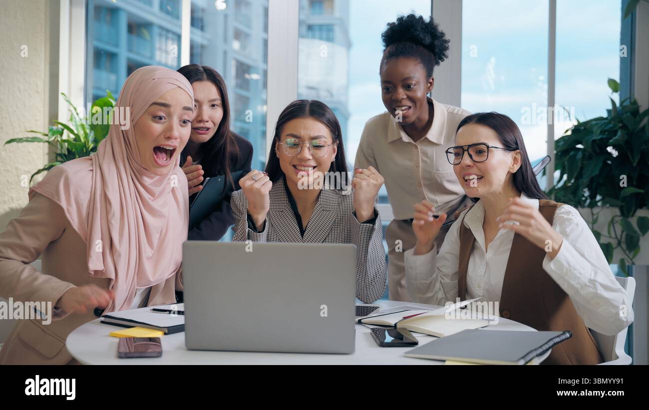 Excité choqué multiethnique femmes femmes d'affaires collègues groupe multiracial cherchant ordinateur portable célébrant l'offre d'affaires de choc gagnant Banque D'Images