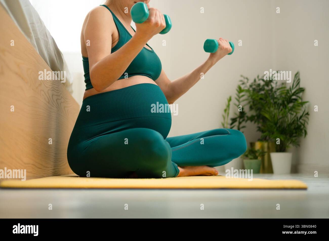 Femme enceinte sereine dans la posture étirée des jambes croisées sur le lit, maintenant la routine de forme physique. Nourrir le corps et l'esprit en attendant l'arrivée de bébé. Banque D'Images