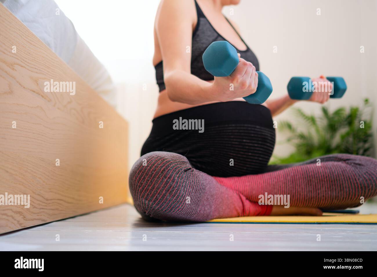 Femme enceinte sereine dans la posture étirée des jambes croisées sur le lit, maintenant la routine de forme physique. Nourrir le corps et l'esprit en attendant l'arrivée de bébé. Banque D'Images