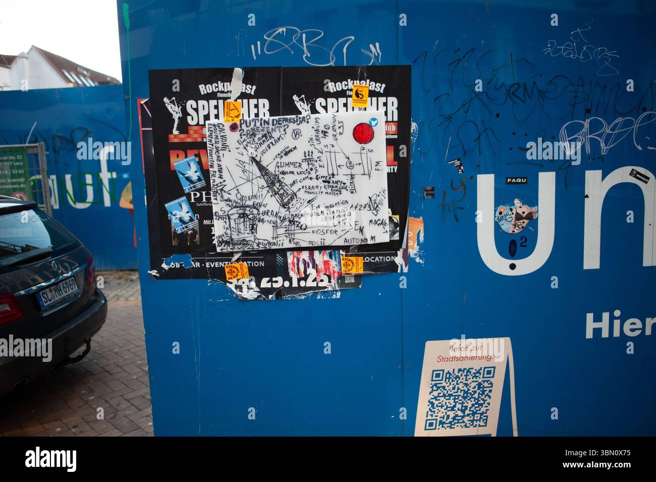 Flensburg, Schleswig-Holstein Blaue Holzwand vor Baustelle in Flensburg, beklebt mit Konzertplakaten und einem weißen, wild beschrifteten Blatt voller politischer Schlagworte, Zeichnungen und Symbolik zu Russland und Atomthemen..Aufnahme vom 29.06.2025, Flensburg. *** Flensburg, Schleswig Holstein mur en bois bleu devant un chantier de construction à Flensburg, collé avec des affiches de concert et une feuille blanche, étiquetée avec beaucoup de slogans politiques, dessins et symbolisme sur la Russie et les questions nucléaires photo prise le 29 06 2025, Flensburg Banque D'Images
