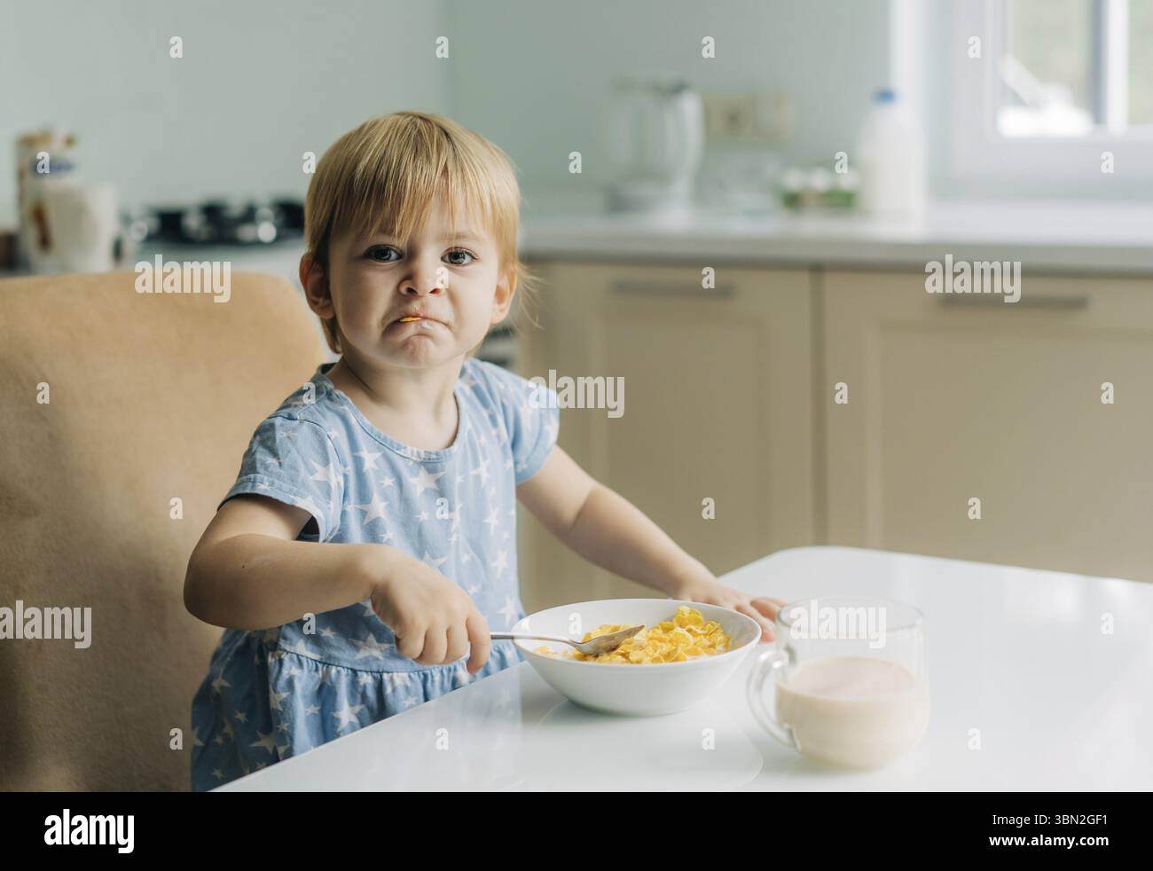 Ein kleines Maedchen im Kleinkindalter isst morgens in der Kueche Cornflakes mit Milch Banque D'Images