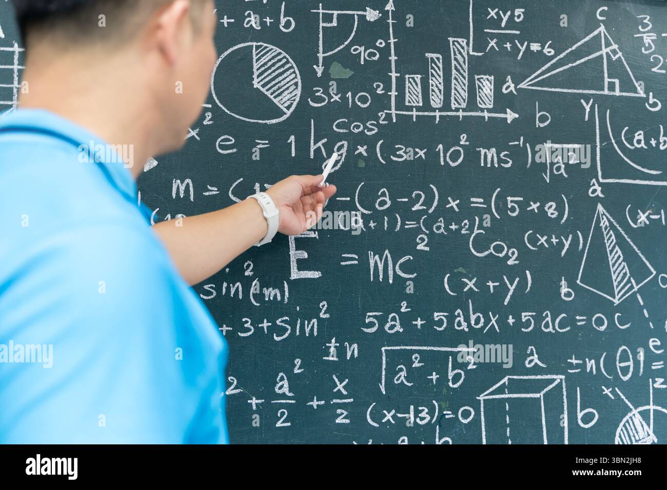 Gros plan d'un professeur en chemise bleue pointant des formules mathématiques sur un tableau pendant la classe. Parfait pour l'éducation, l'école, académique, l'instruction, te Banque D'Images