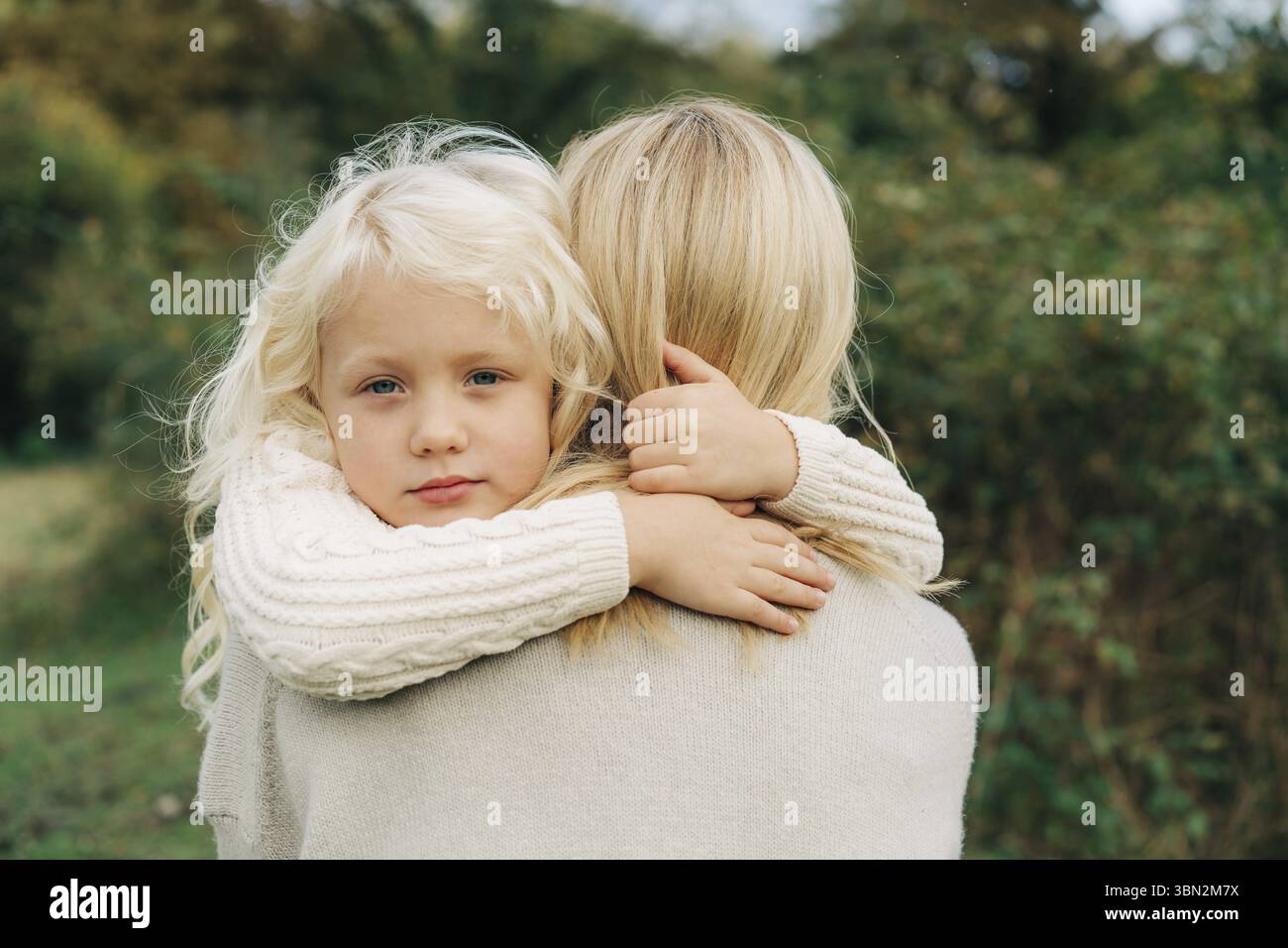 Ein kleines blondes Maedchen liegt in den Armen seiner Mutter und drueckt ihren Hals Banque D'Images