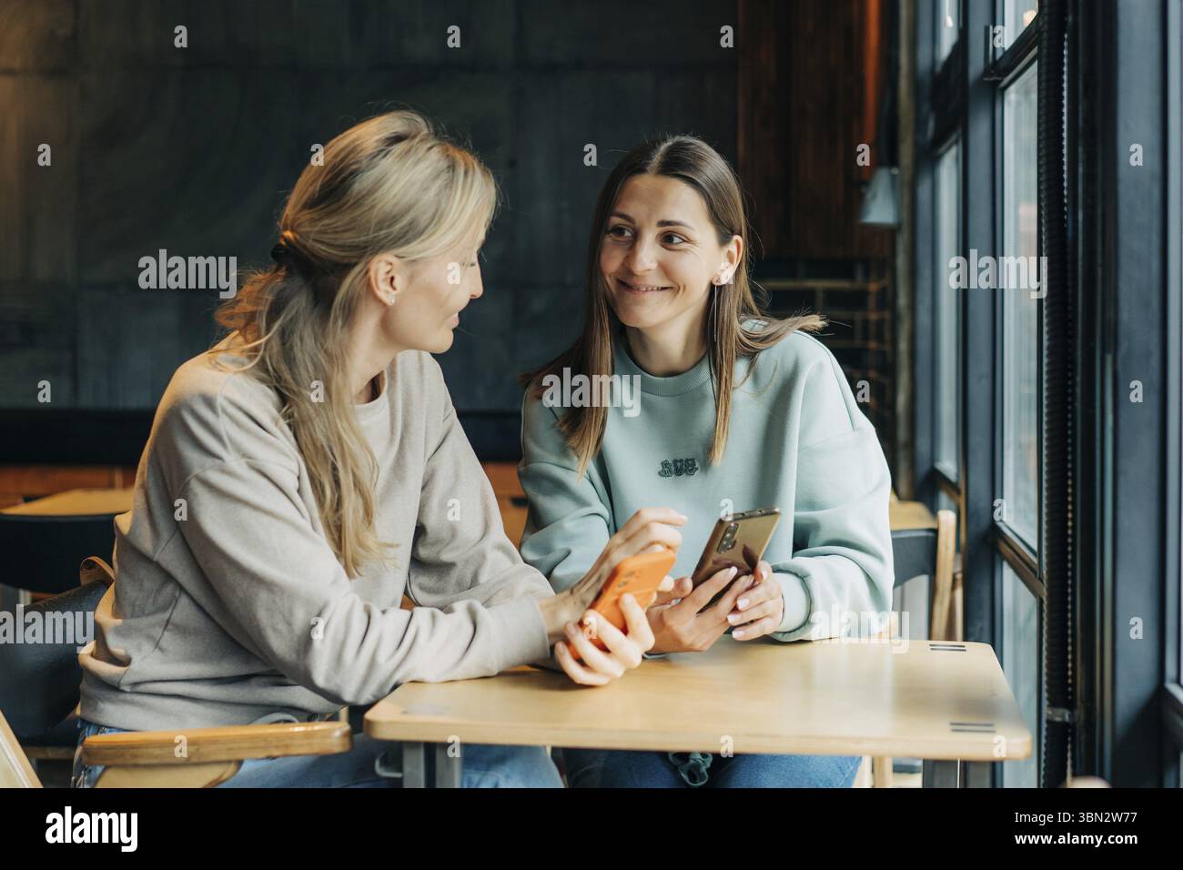 Zwei Freundinnen sitzen in einem Cafe und sehen sich Online-Medien auf dem Telefon an und lachen Banque D'Images