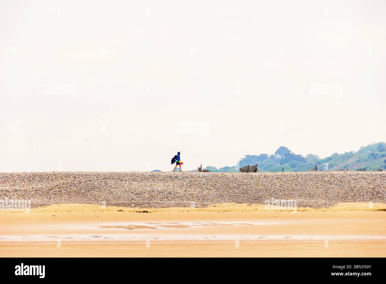 Homme marchant sur une digue avec des galets près d'une plage de sable Banque D'Images
