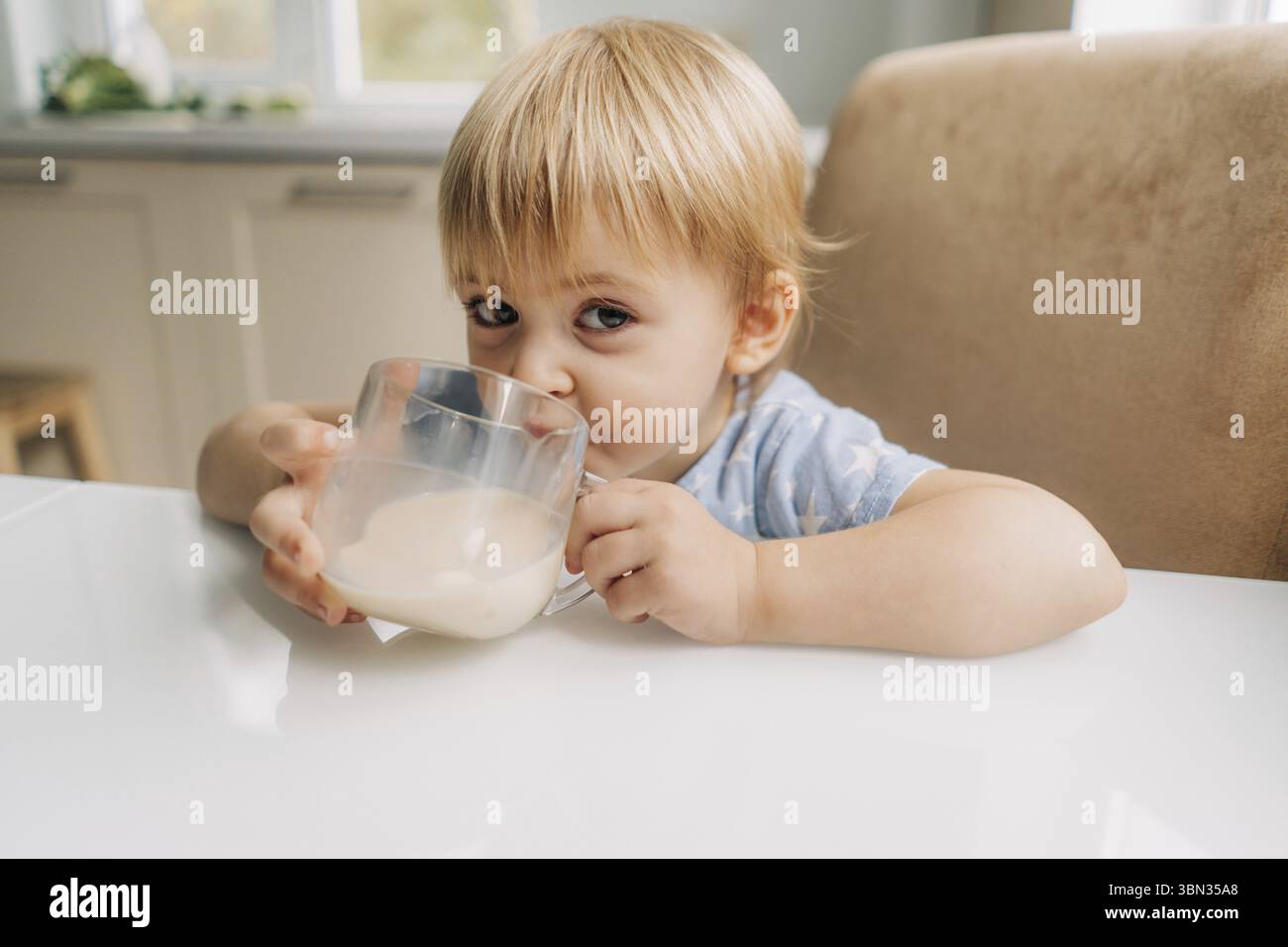 Ein kleines Maedchen trinkt zu Hause in der Kueche koestliche frische Milch aus einem Becher Banque D'Images