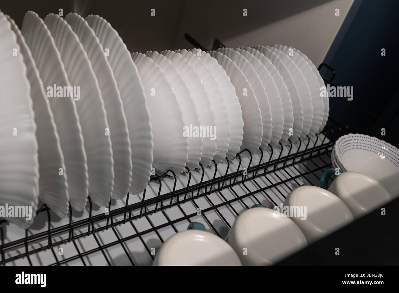 La vaisselle propre est soigneusement disposée dans une grille, séchant après avoir été lavée. La cuisine présente un design contemporain avec des assiettes et des tasses blanches de manière organisée. Banque D'Images