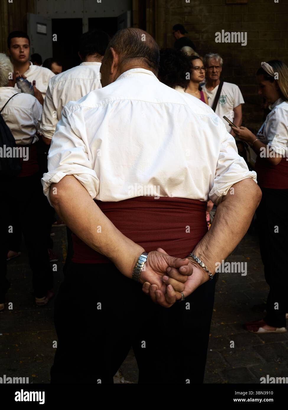 Un homme se tient debout, les mains serrées derrière son dos, portant une chemise blanche et une ceinture marron, parmi un groupe de personnes vêtues de la même façon. La scène Tak Banque D'Images