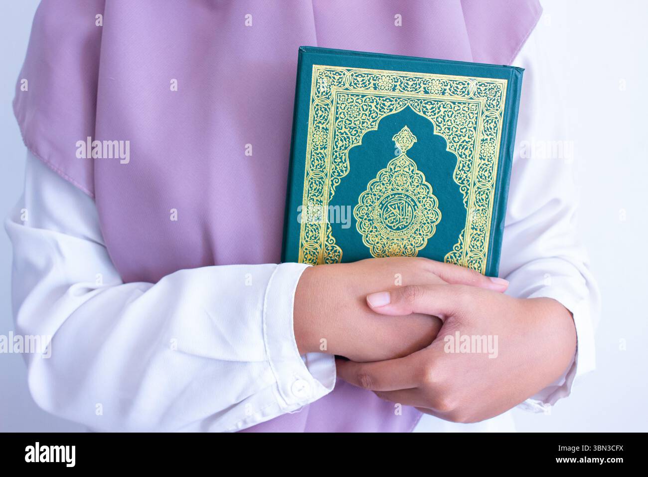 Une femme musulmane portant une robe musulmane blanche tient un livre sacré musulman Al-Qur'an sur sa poitrine. La couverture du livre est écrite comme 'Al-Qur'anul Karim' Banque D'Images