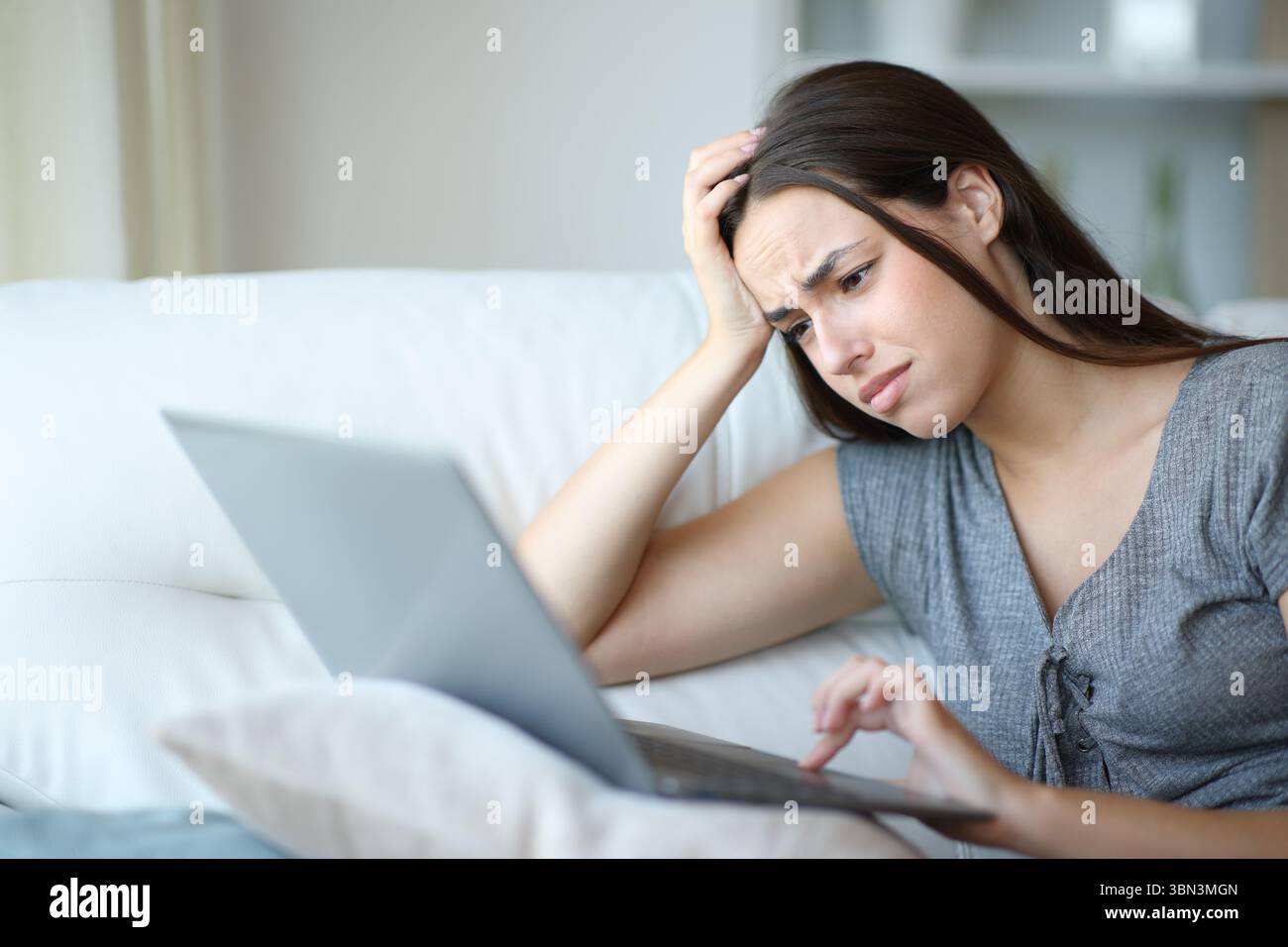 Femme stressée vérifiant les mauvaises nouvelles sur un ordinateur personnel assis sur un canapé à la maison Banque D'Images