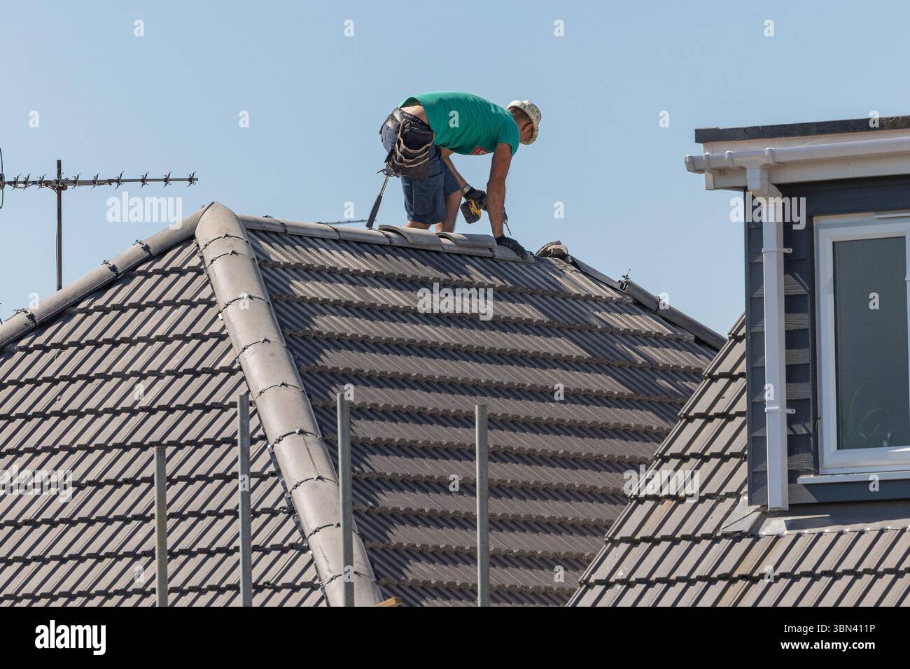 Un ouvrier de la construction fixant les tuiles faîtières à un toit de maison de nouvelle construction. Banque D'Images