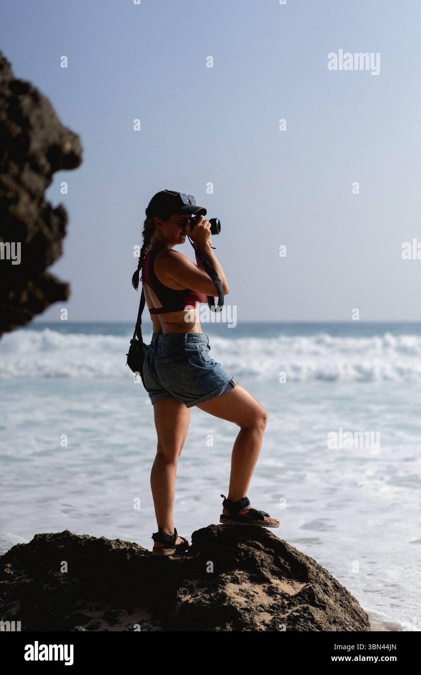 Femme avec caméra debout sur le rocher près de l'océan Banque D'Images