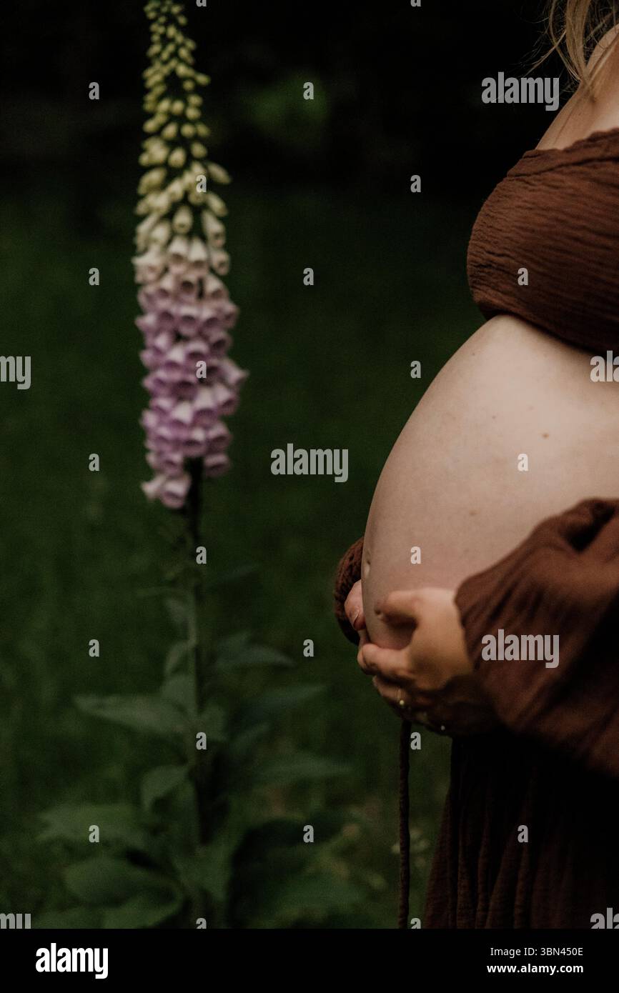 Femme enceinte en robe brune debout parmi les fleurs sauvages Banque D'Images