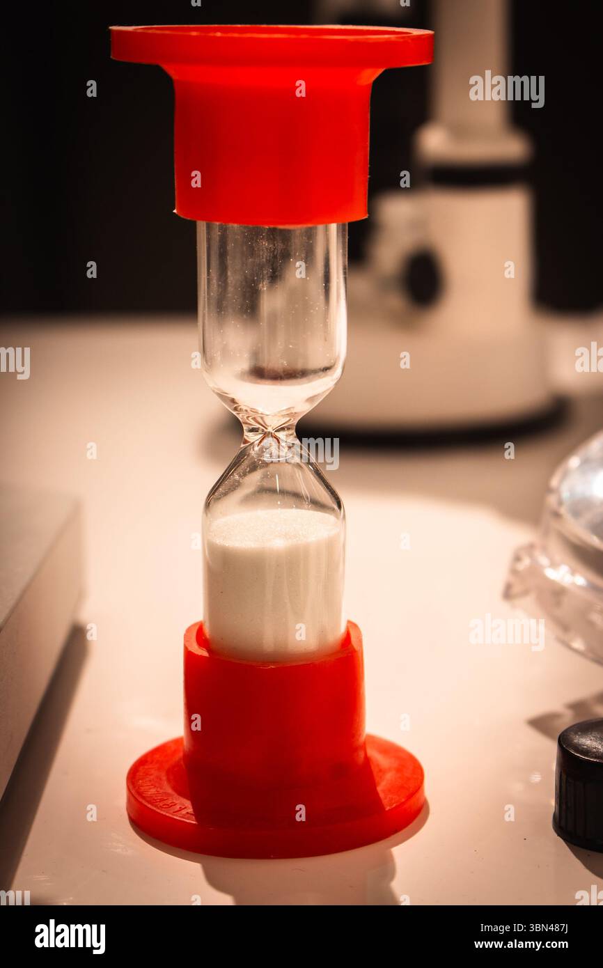 Petit sablier rouge avec du sable blanc sur la table. Sablier sur table de laboratoire. Concept de passage du temps. EQUIPEMENT de mesure du temps. Horloge vintage. Minuterie rétro. Banque D'Images