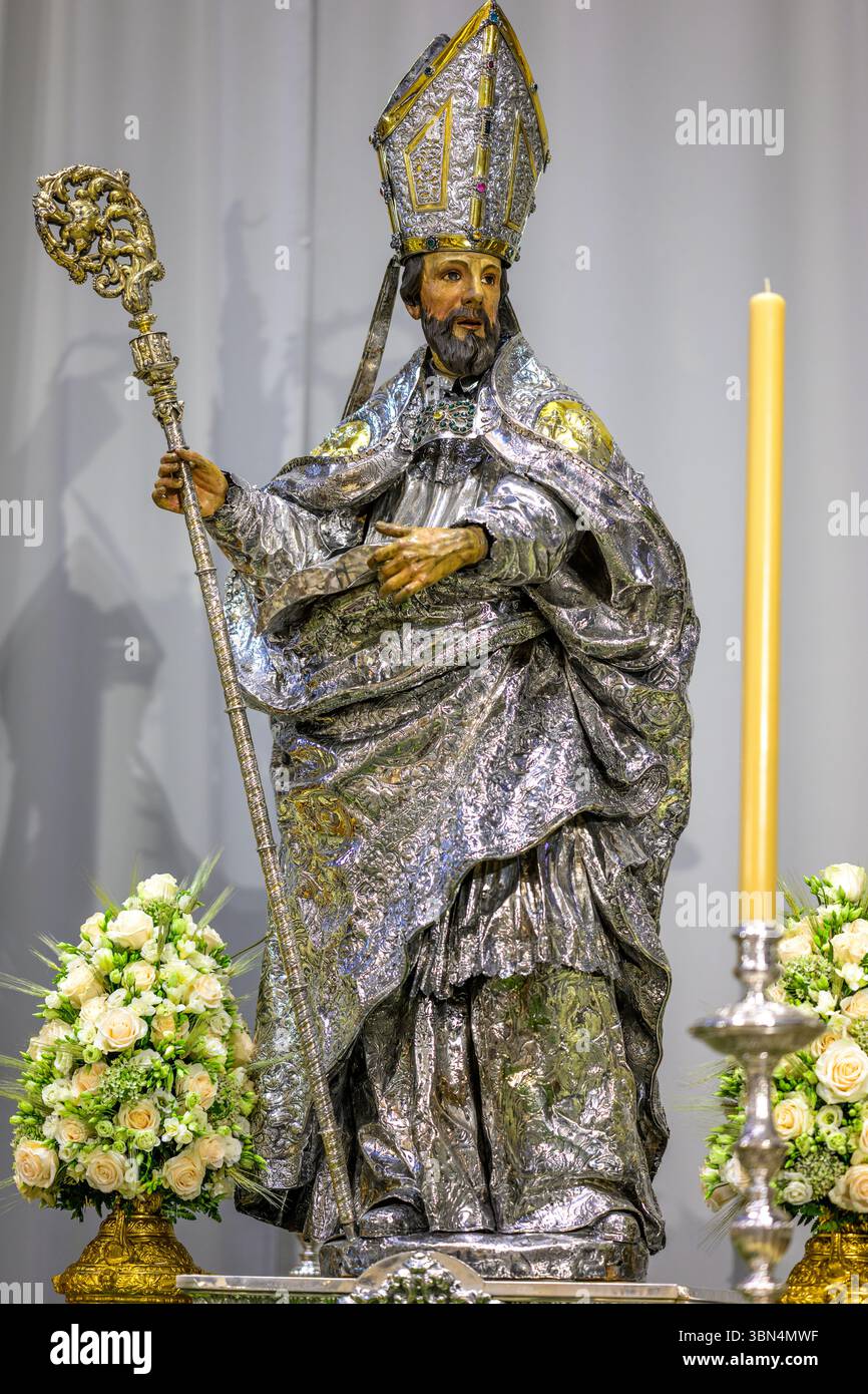Cette sculpture polychrome de Saint Isidore se dresse dans la cathédrale de Séville, ornée de vêtements argentés et entourée de fleurs et de bougies. Banque D'Images