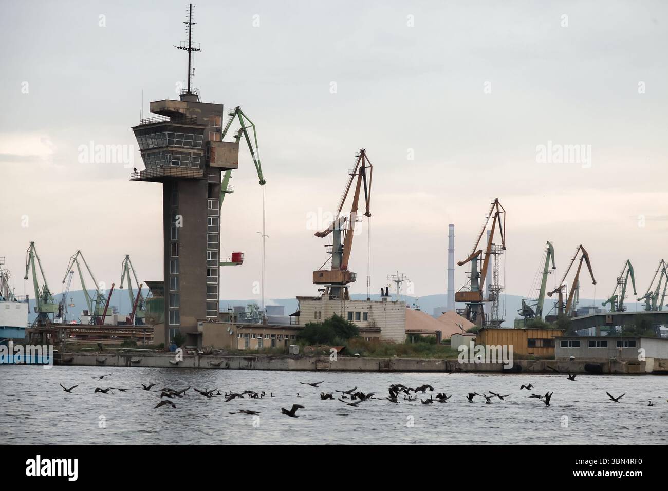 Une vue panoramique sur un port industriel de Varna avec des grues, une tour de guet, les entrepôts environnants et les reflets de l'eau. Côte de la mer Noire, Bulgarie Banque D'Images