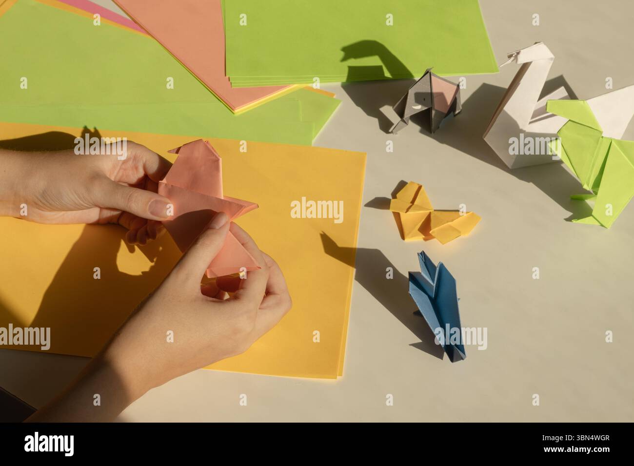 Mains pliant des animaux en papier colorés sur une table avec diverses figures d'origami et des feuilles de papier Banque D'Images