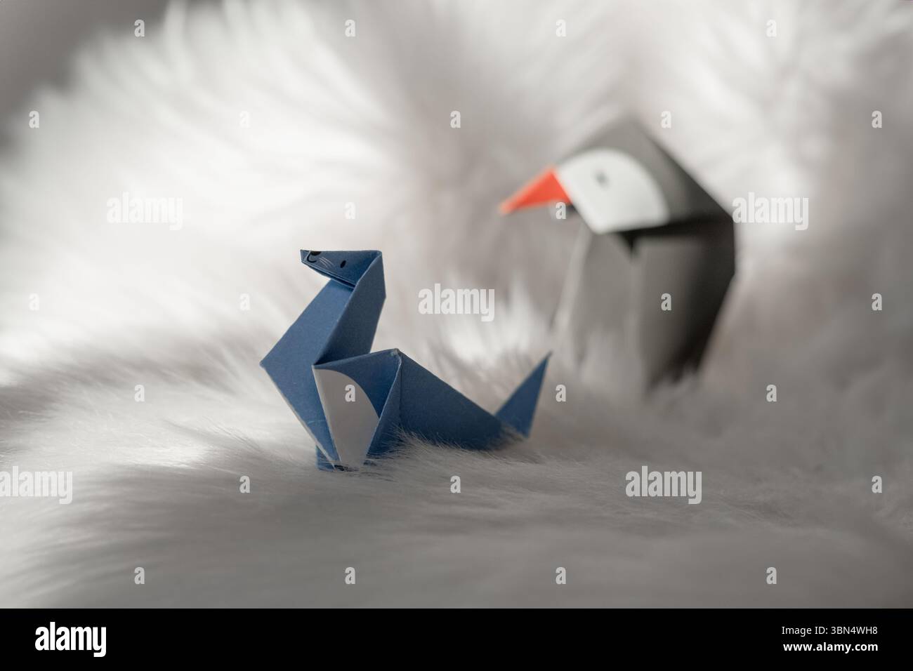 Deux animaux en papier pliés — un sceau bleu et un pingouin — placés sur une fourrure blanche douce, concept artistique fait à la main Banque D'Images
