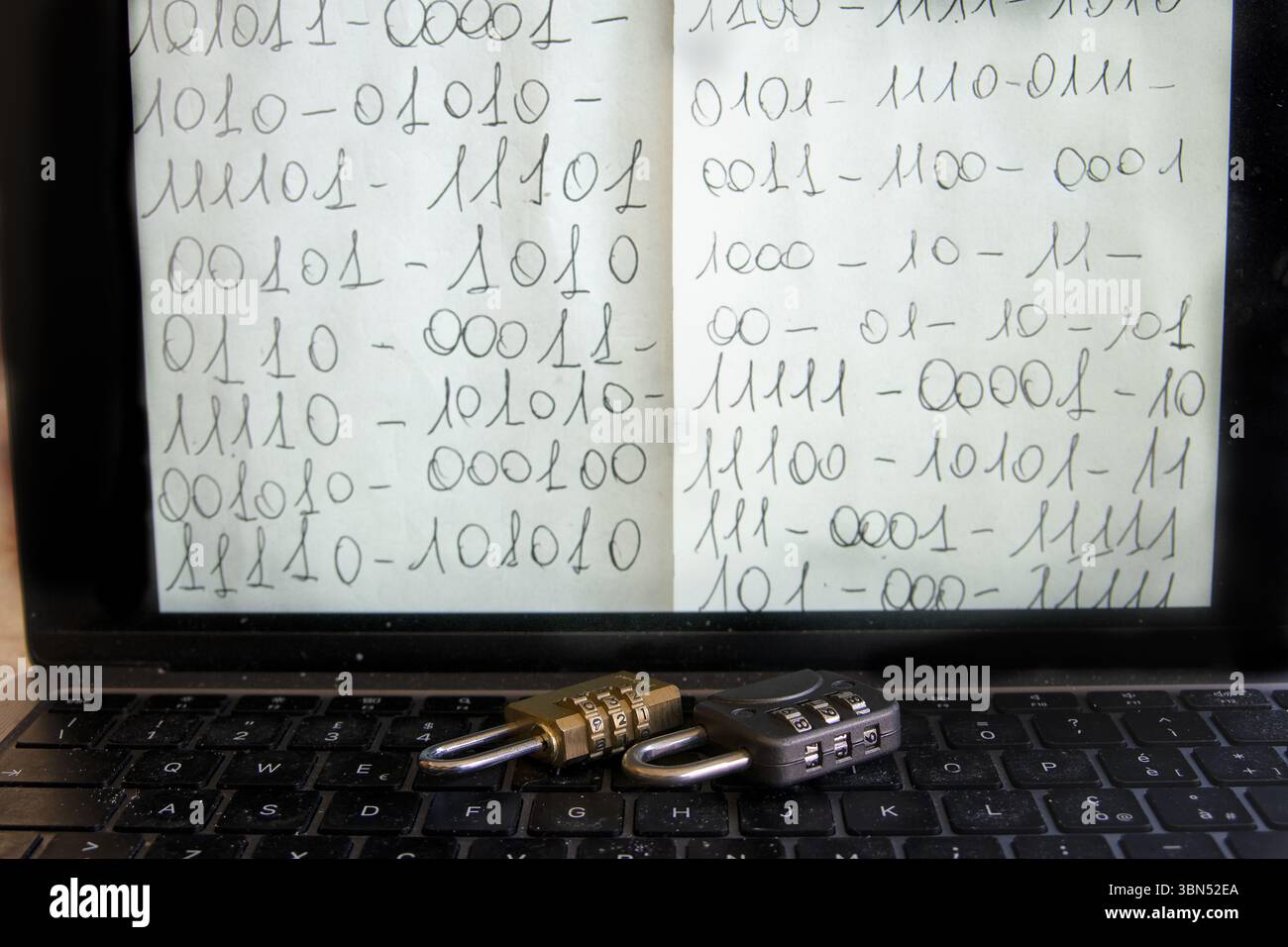 ordinateur portable ouvert affichant un code binaire manuscrit à l'écran avec deux cadenas à combinaison sur le clavier, symbolisant la protection des données numériques Banque D'Images