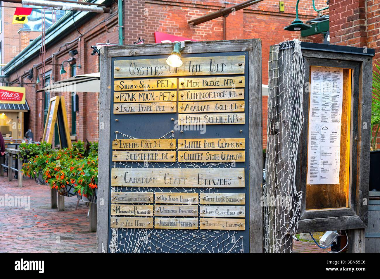 Un panneau rustique dans le Distillery District énumère les variétés d'huîtres et les brasseries artisanales utilisant des lattes en bois gravées, encadrées par un filet de pêche et un a chaud Banque D'Images