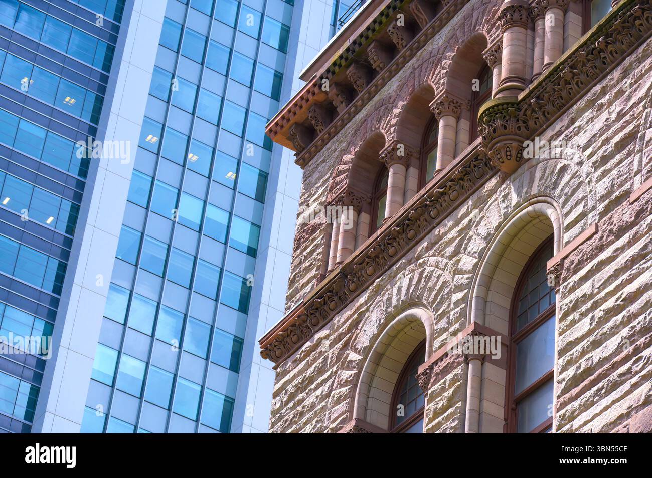 Une section de l'ancien hôtel de ville montre des murs en pierre brute, des fenêtres cintrées et des colonnes romanes sculptées, contrastant fortement avec la façade en verre lisse de Banque D'Images