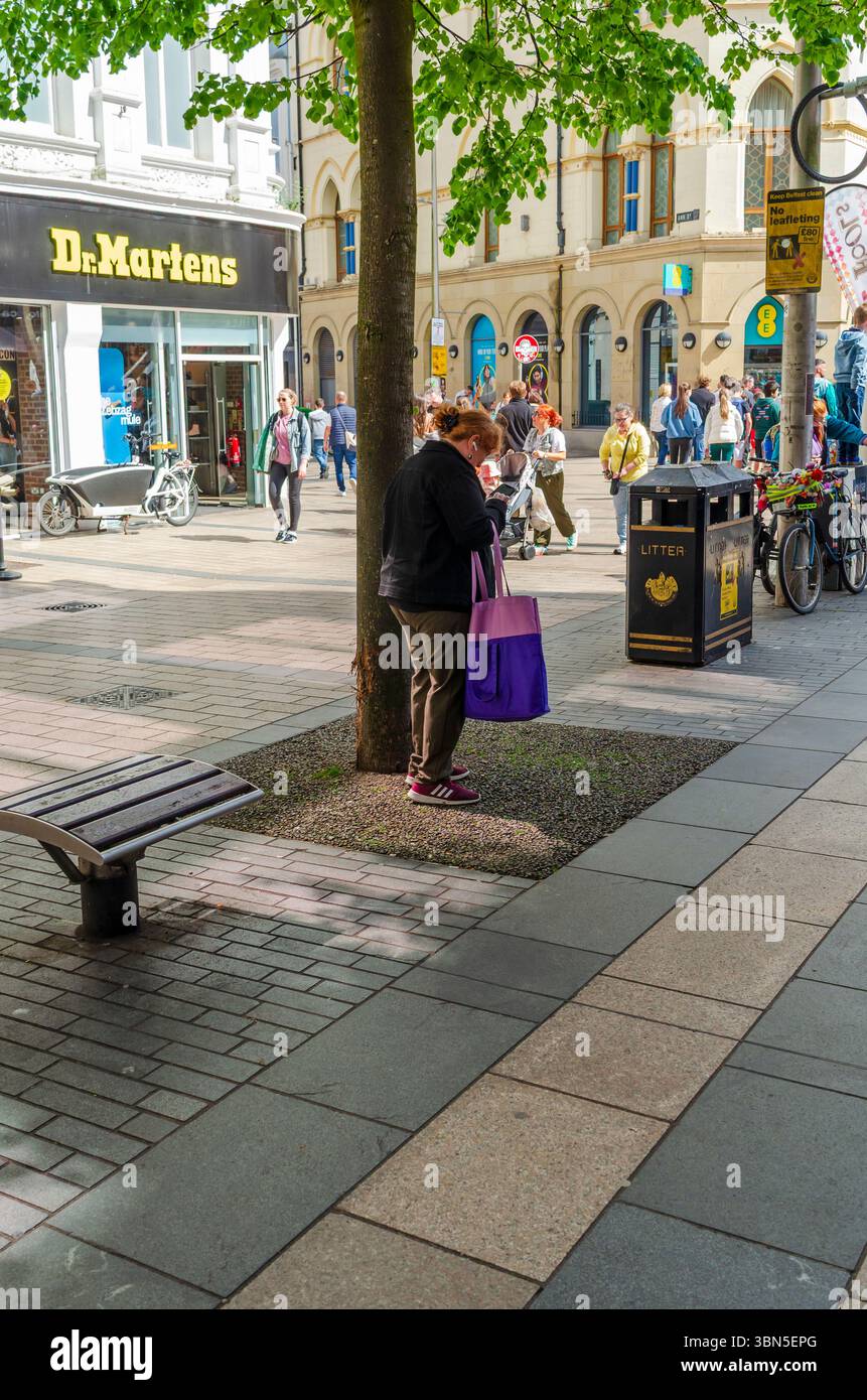 Belfast Co.Antrim mai 03 2025 - femme regardant dans un sac à provisions sous un arbre dans le centre-ville avec des acheteurs passant par Banque D'Images