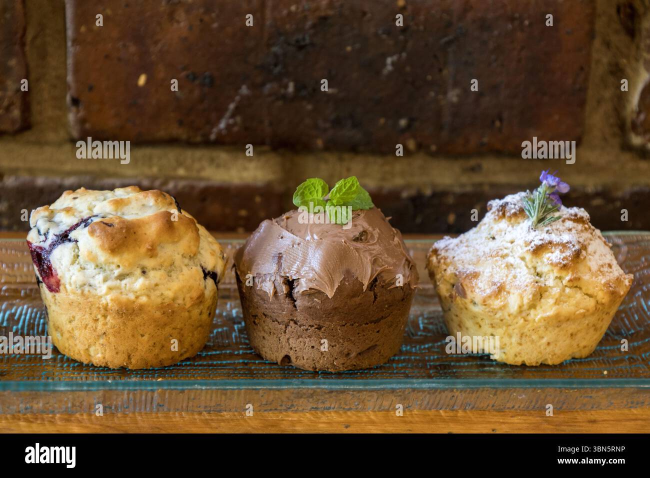 Trois saveurs différentes (myrtille, chocolat-menthe et romarin) de muffins faits maison sur un fond brun rustique. Banque D'Images