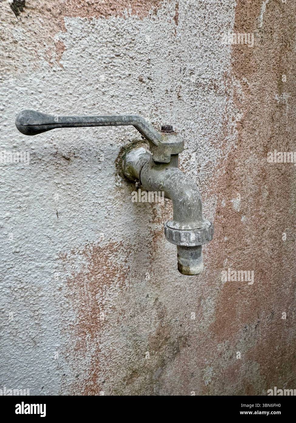 Robinet d'eau extérieur altéré monté sur un mur en stuc texturé. - Image de stock capturée avec un smartphone