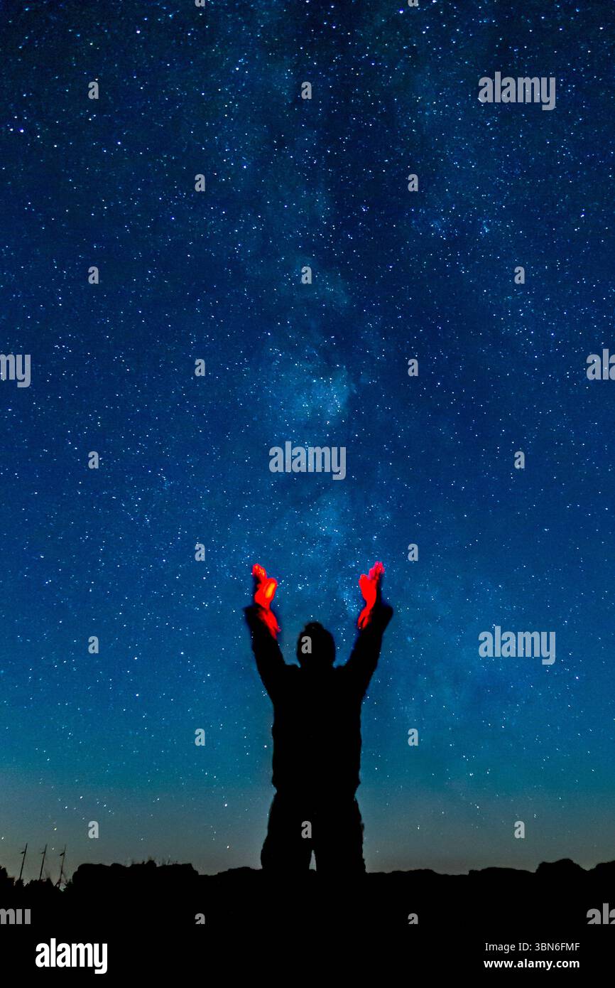 Cove Palisades State Park, Oregon, USA - 31 août 2018 : une personne est silhouettée contre le ciel nocturne, tenant des lumières rouges jusqu'aux étoiles. Banque D'Images