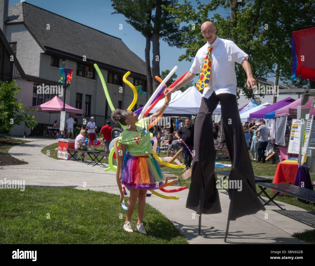 Lors de l'événement Peekskill Pride Family Pride in the Park, un homme sur pilotis rencontre une dame portant des couleurs de fierté et beaucoup de ballons. Banque D'Images