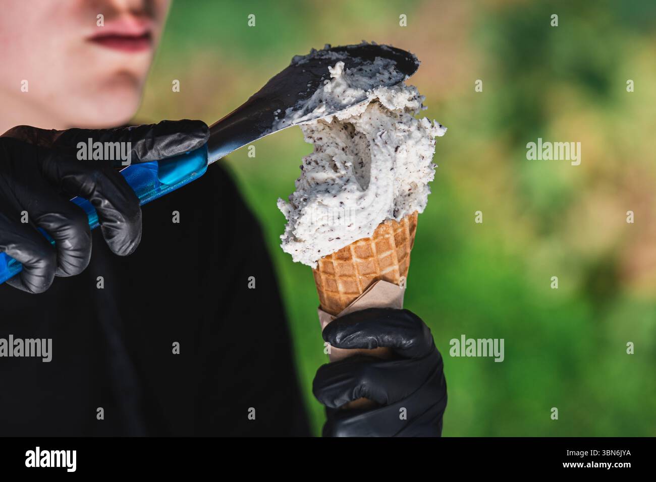 Gros plan d'une personne portant des gants noirs servant une généreuse boule de stracciatella (vanille avec flocons de chocolat) crème glacée dans un cône de gaufre Banque D'Images