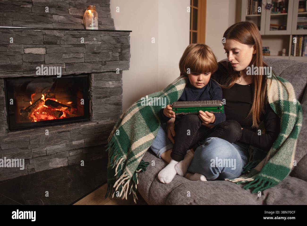 Mère et fils plying avec jouet sur un canapé près de la cheminée dans un intérieur confortable de la maison. Un moment chaleureux en famille dans le salon. Fils et maman heureux. Banque D'Images